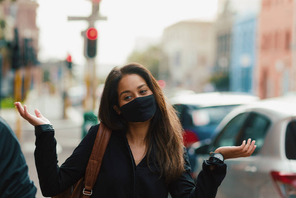 Young confused woman wearing face mask on city street - Foto, Imagen