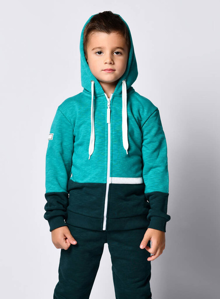 Little brunette kid in colorful tracksuit and sneakers on a gray background. - Foto, afbeelding
