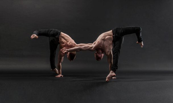 kaksi kaksoisveljeä mustissa farkuissa, joissa on alaston vartalo, suorittavat akrobaattisia elementtejä, mustaa taustaa - Valokuva, kuva