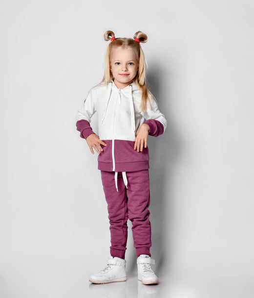 Little blonde girl in a sports suit posing on a gray background. - Photo, image