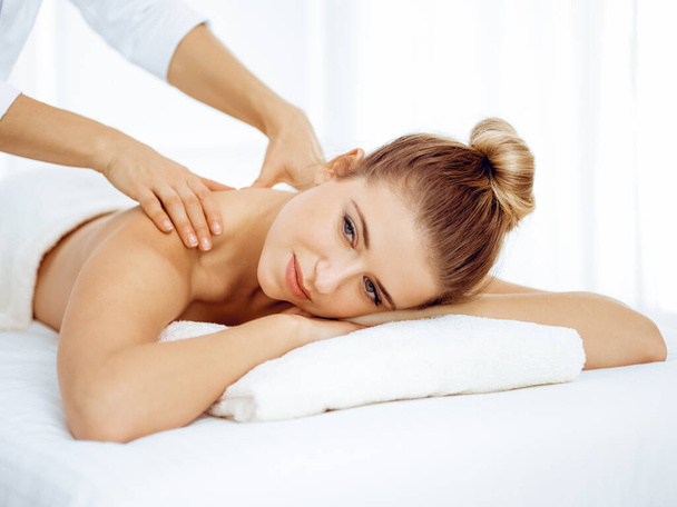 Jonge en blonde vrouw geniet van massage van rug in spa salon. Schoonheidsconcept - Foto, afbeelding