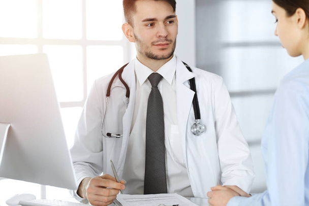 Doctor and patient. Physician man filling up medication history records form while sitting at the glass desk in medical office or clinic. Medicine and healthcare concept - Zdjęcie, obraz