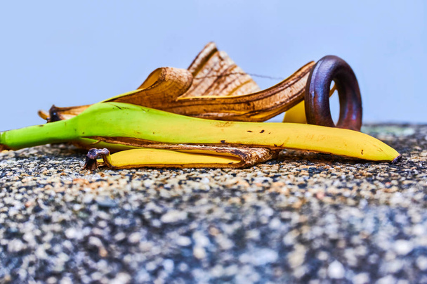 View to a banana peel lying on a concrete bollard with pebbles next to a metal ring. - Фото, изображение