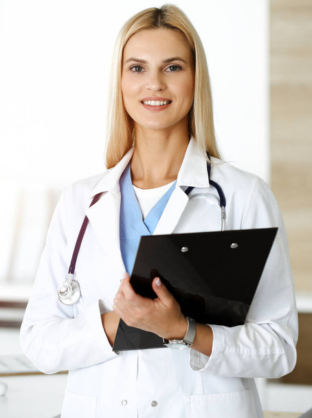 Doctor woman controls medication history records and exam results while using clipboard in sunny hospital . Medicine and healthcare concept - Foto, immagini