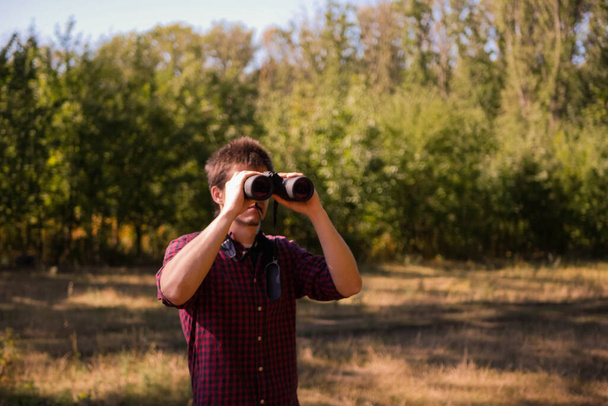 Muž v kostkovaném krátkém pohledu dalekohledem. Lesní turistika. Pozorování ptáků. Hledám koncept příležitostí. Dobrodružné hledání  - Fotografie, Obrázek
