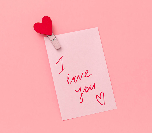 pink paper note with hand writing text i love you and cloth pin decorated with red heart on a vibrant yellow background - Photo, image