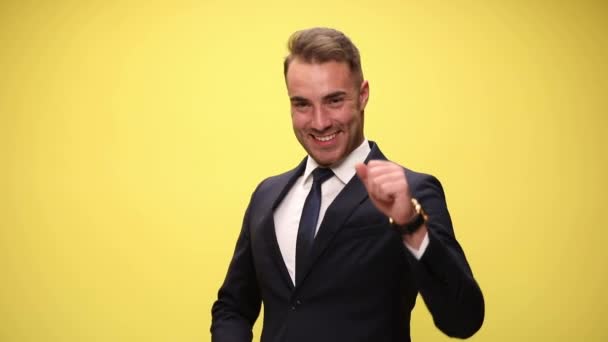 aantrekkelijke zakenman glimlachend naar de camera, dansend rond met zijn armen en zijn lichaam, omhoog wijzend en met een goede tijd op gele achtergrond - Video