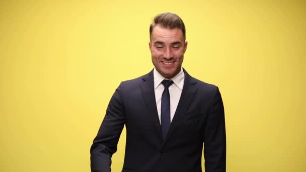 joven hombre de negocios guapo con traje azul marino de pie y la mano temblorosa sobre fondo amarillo - Metraje, vídeo