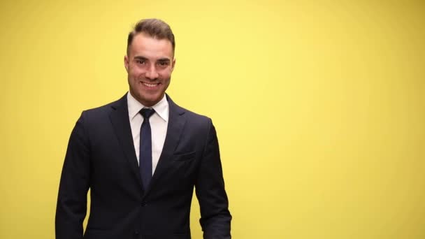 young businessman with a wide smile on his face showing something aside then pointing at camera on yellow background - Footage, Video