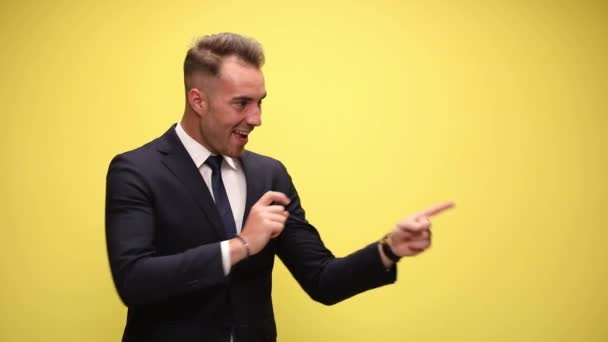 businessman pointing repeatedly to a side, pointing up and giving a thumbs up on yellow background - Footage, Video