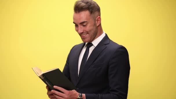 молодой бизнесмен читает свою книгу и очень взволнован ею, поднимая большой палец вверх на желтом фоне - Кадры, видео