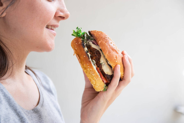 Κοντινό πορτρέτο μιας πεινασμένης νεαρής γυναίκας που τρώει μπέργκερ σε λευκό φόντο - Φωτογραφία, εικόνα