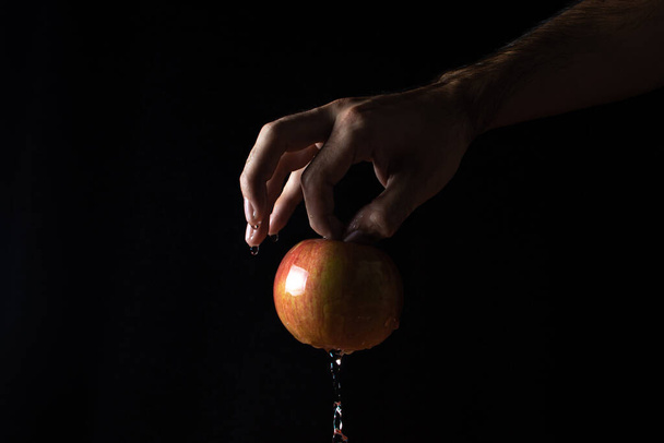 水は黒い背景にリンゴを流れ落ちる。手にリンゴがある。ぬれたリンゴ - 写真・画像