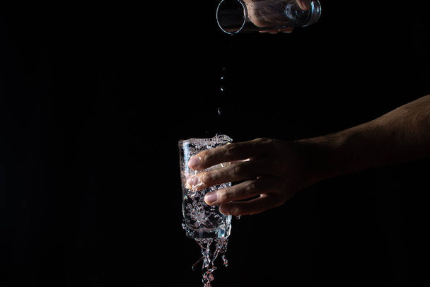 Water on a black background. A glass overflowing with water. Water is poured out of the glass. Pure water - Foto, Imagem