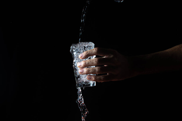 Νερό σε μαύρο φόντο. Ένα ποτήρι ξεχειλίζει με νερό. Νερό χύνεται από το ποτήρι. Καθαρό νερό - Φωτογραφία, εικόνα