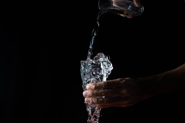 Water on a black background. A glass overflowing with water. Water is poured out of the glass. Pure water - Foto, Bild