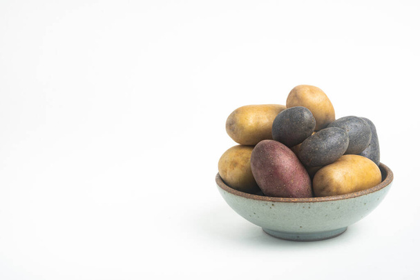 Eine sortierte Farbe rohe und frische Kartoffeln kunstvoll auf einer Schüssel angeordnet und auf weißem Hintergrund gesetzt. - Foto, Bild