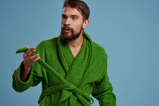 Bearded man in green robe with belt on blue background cropped view of emotion - Photo, Image