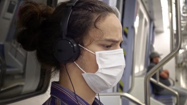 Maskovaný smutně vypadající přemýšlivý teenager poslouchající hudbu se sluchátky uvnitř metra se sociálně distancovanými lidmi - Záběry, video
