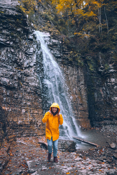 portrait of woman in yellow raincoat in front of autumn waterfall hiking concept - Fotografie, Obrázek
