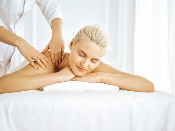 Beautiful blonde woman enjoying back massage with closed eyes. Spa salon concept - Фото, зображення