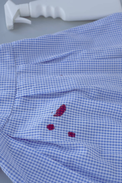 schmutzige Blutflecken auf dem Kleid und Fleckenentferner. Isoliert auf grauem Hintergrund. Hochwertiges Foto - Foto, Bild