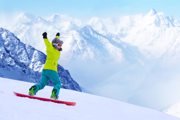 Girl snowboarder running down the slope in Alpine mountains. Winter sport and recreation, leisure outdoor activities. Image of excited screaming young woman enjoyment concept - Photo, Image