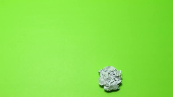 crumpled paper ball on green background. The screen wrinkles as a ball of paper and leaves the screen jumping. And, a sheet of paper enters the screen as a ball and unwrap itself filling the screen. - Footage, Video