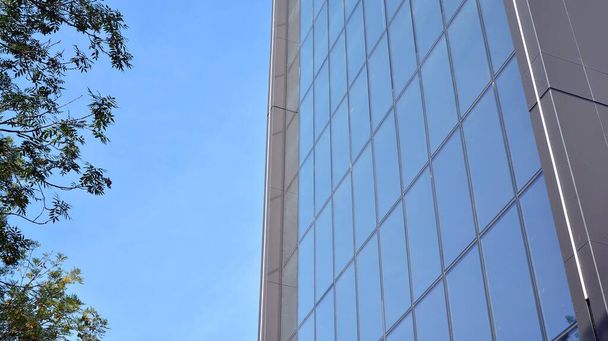 Μπλε τοίχος κουρτίνας από τονισμένο γυαλί και μεταλλικές κατασκευές κάτω από τον γαλάζιο ουρανό. Ένα θραύσμα ενός κτιρίου. - Φωτογραφία, εικόνα