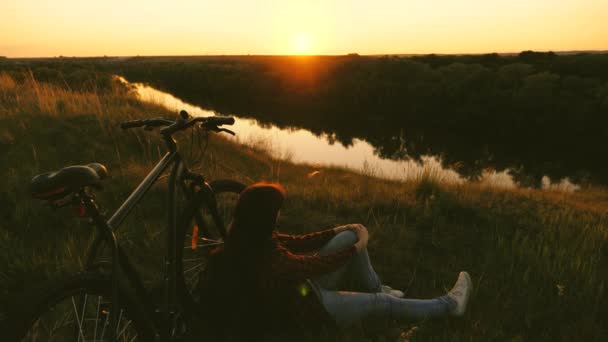 concepto de aventura y viajes. ciclista soltera descansando en el parque. chica libre viaja con una bicicleta en la puesta del sol. Senderista joven y saludable sentada en la colina junto a la bicicleta, disfrutando de la naturaleza y el sol. - Imágenes, Vídeo