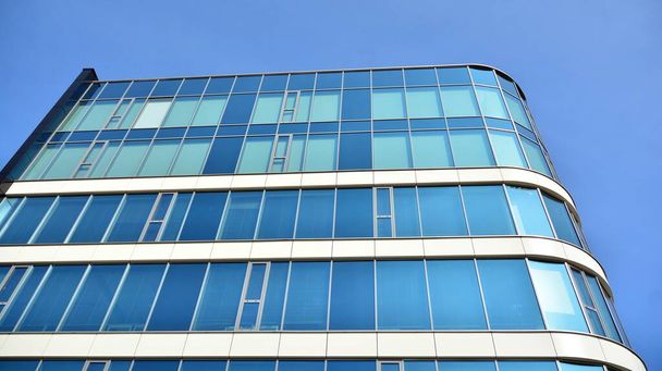 Blauwe gordijnwand gemaakt van gehard glas en stalen constructies onder blauwe hemel. Een fragment van een gebouw. - Foto, afbeelding