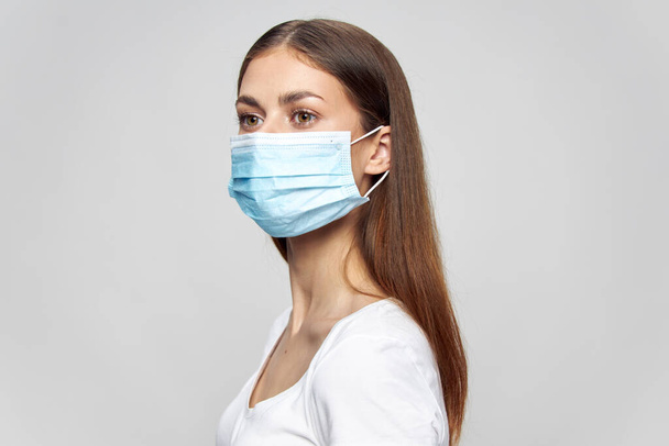 Frau in medizinischer Maske schaut zur Seite auf isoliertem Hintergrund in weißem T-Shirt - Foto, Bild