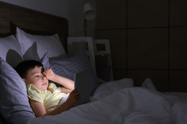 Little boy suffering from sleep disorder with tablet computer in bedroom - Fotó, kép