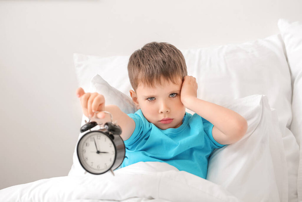 Little boy suffering from sleep disorder with alarm clock in bedroom - Photo, Image