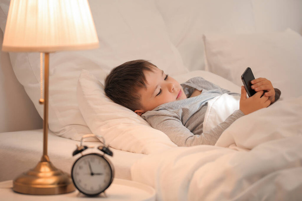 Petit garçon souffrant de troubles du sommeil avec téléphone portable dans la chambre - Photo, image