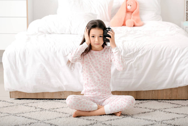 Klein meisje lijdt aan slaapstoornis met wekker in de slaapkamer - Foto, afbeelding