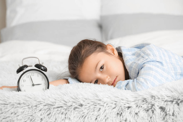 Little girl suffering from sleep disorder with alarm clock in bedroom - Foto, Imagem