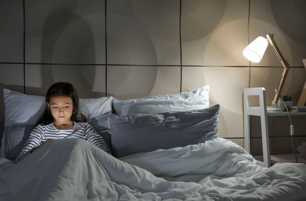 Маленькая девочка страдает расстройством сна с планшетным компьютером в спальне - Фото, изображение