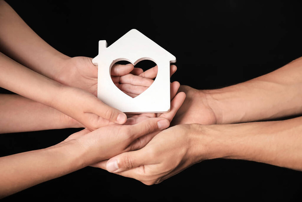 Hands of family with small house on dark background - Foto, Bild