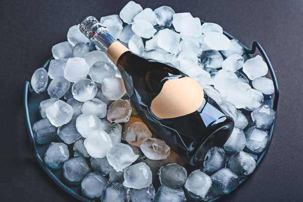 Bottle of champagne and ice cubes on dark background - Photo, Image