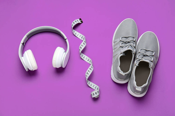 Sportive shoes, measuring tape and headphones on color background. Weight loss concept - Foto, Bild