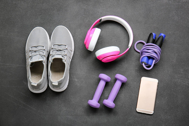 Sportovní obuv, činky, skákací lano, mobilní telefon a sluchátka na šedém pozadí - Fotografie, Obrázek