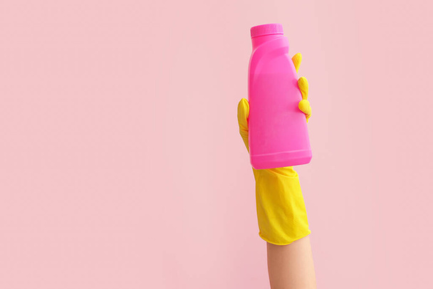Hand in rubber glove holding detergent on color background - Foto, imagen