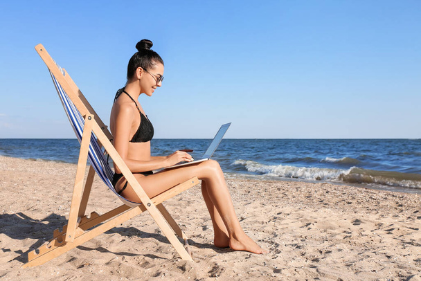 Beautiful young woman with laptop on sea beach - Fotó, kép