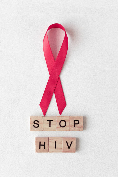 Concetto per la Giornata Mondiale dell'AIDS. Nastro rosso vicino a lettere di legno. Fermare le parole HIV. - Foto, immagini