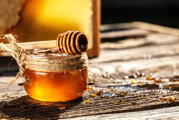 Honig tropft aus einem hölzernen Honiglöffel in einem Glas auf rustikalem Holzgrund. Waben mit vollen Honigzellen. Banner, Menü, Rezept, Platz für Text, - Foto, Bild