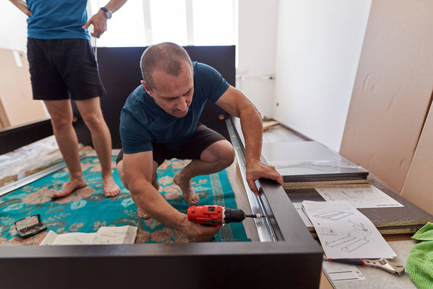 Father helping his son assembly and build the furniture in his new home - 写真・画像