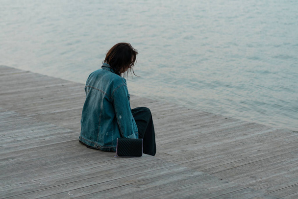 young beautiful woman sits on a wooden bridge near the lake - Foto, Bild