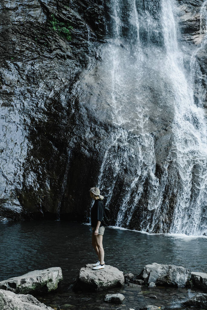 mujer joven en el fondo de una cascada de montaña con una cola de caballo  - Foto, imagen