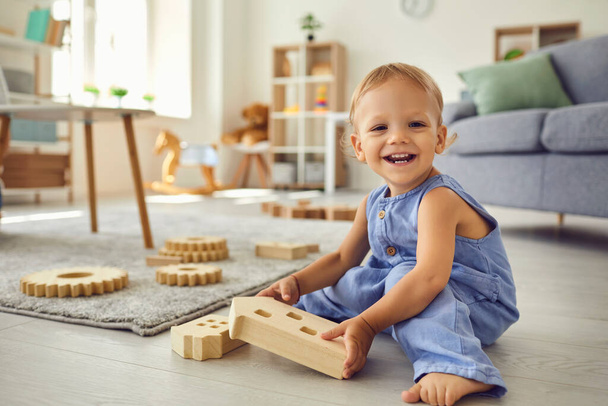Nettes kleines Kind, das glücklich in die Kamera lächelt, während es im gemütlichen Kinderzimmer spielt - Foto, Bild
